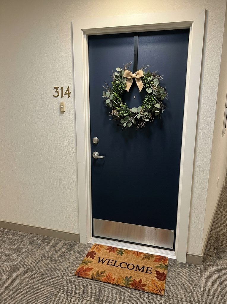  Apartment hallway door with an over-the-door wreath hanger, simple wreath, and seasonal doormat